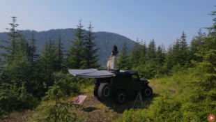 Girl standing on the roof of her Jeep Wrangler looking off into the distance