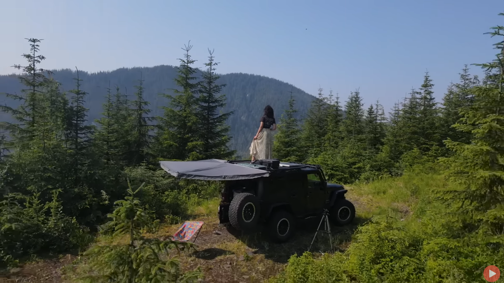 Girl standing on the roof of her Jeep Wrangler looking off into the distance